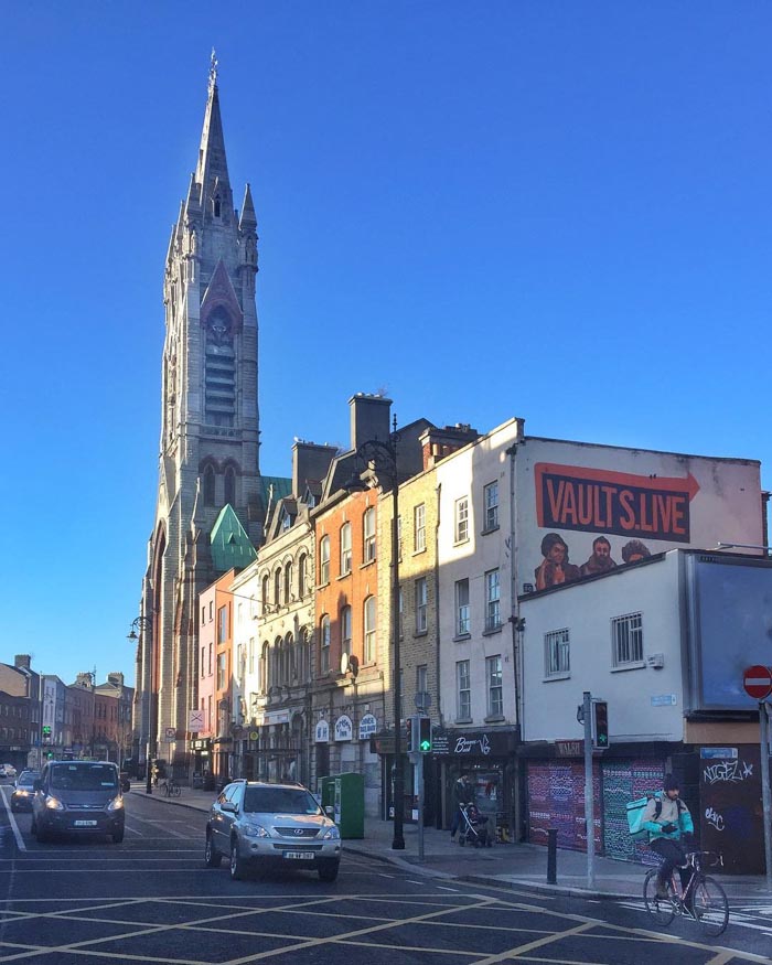 City street with historic buildings and a tall church tower under clear sky, highlighting countries that sleep the most.