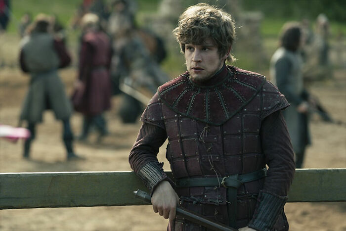 Young knight in medieval armor leaning on a wooden fence, scene from A Knight Of The Seven Kingdoms plot.