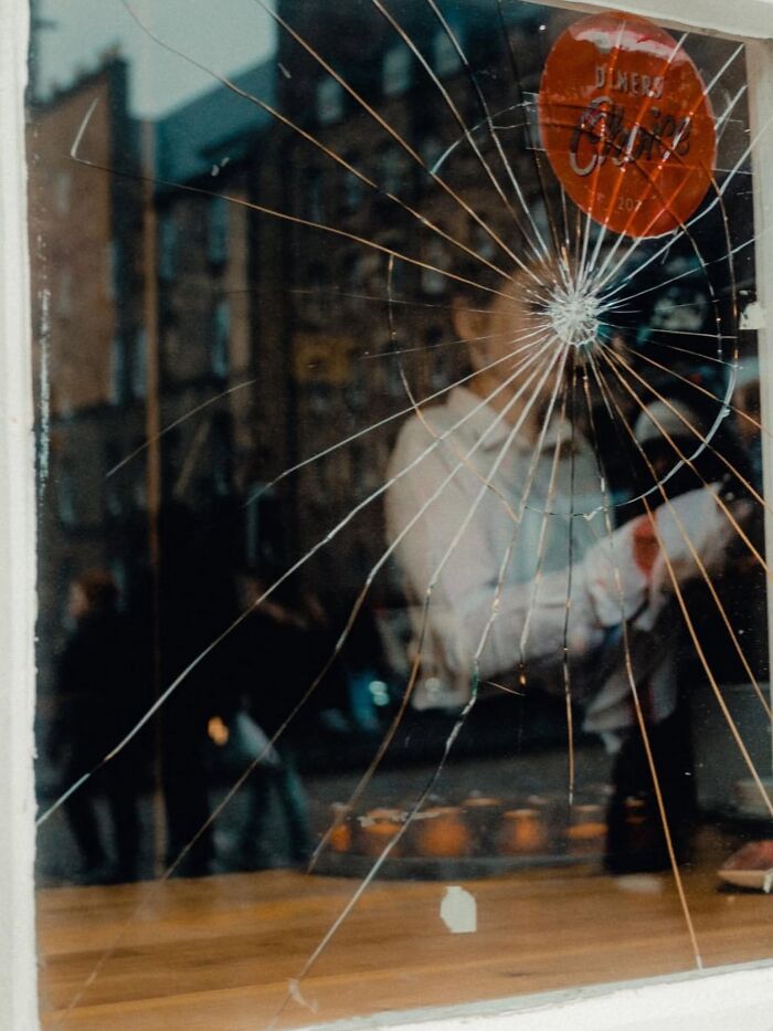 Broken glass window reflecting street life and people, capturing unexpected and beautiful moments in a street photo.