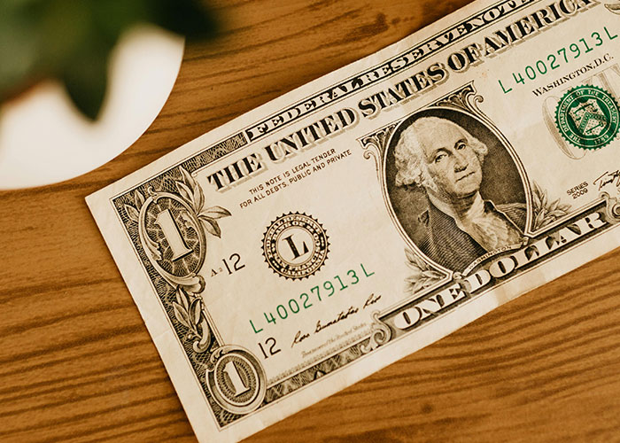 One dollar bill on a wooden table, illustrating money in stories shared by people with wacky experiences.