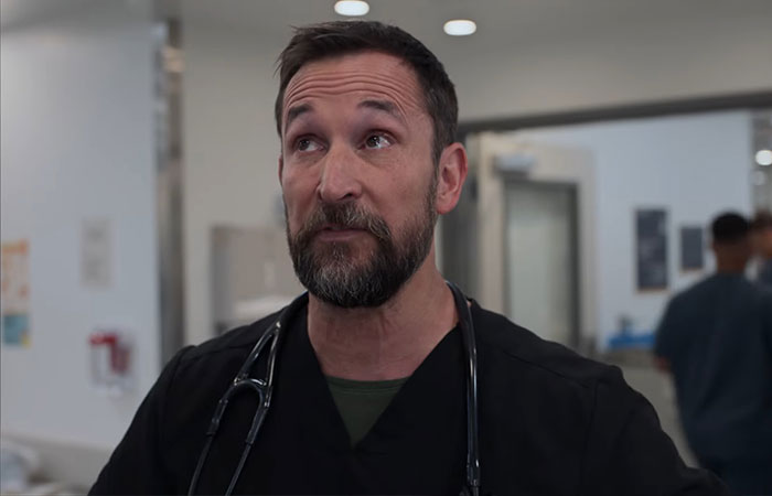 Man in black medical scrubs with stethoscope, inside hospital hallway, related to 2901 meaning in The Pitt Season 2 ending.