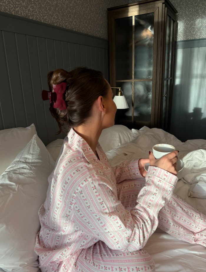 Woman in patterned pajamas sitting on bed holding a cup, illustrating myths vs reality about women needing more sleep than men.