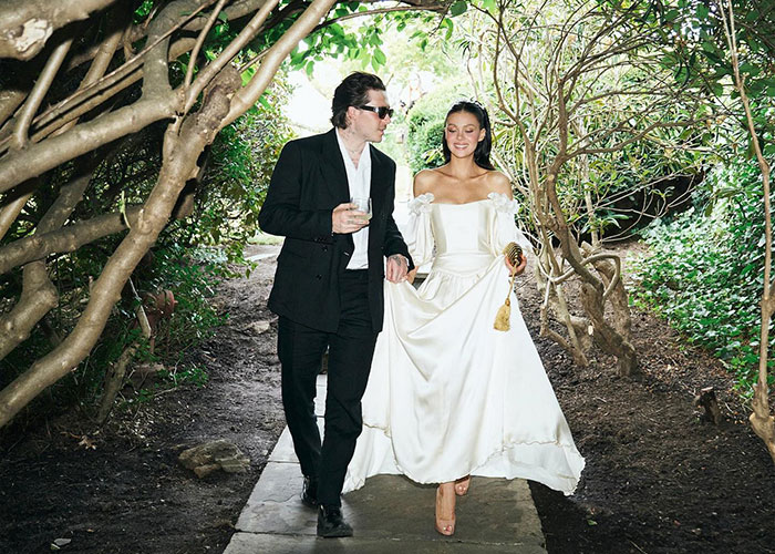 Victoria Beckham walking in a white dress with a man in black suit, footage related to Victoria Beckham dance controversy.