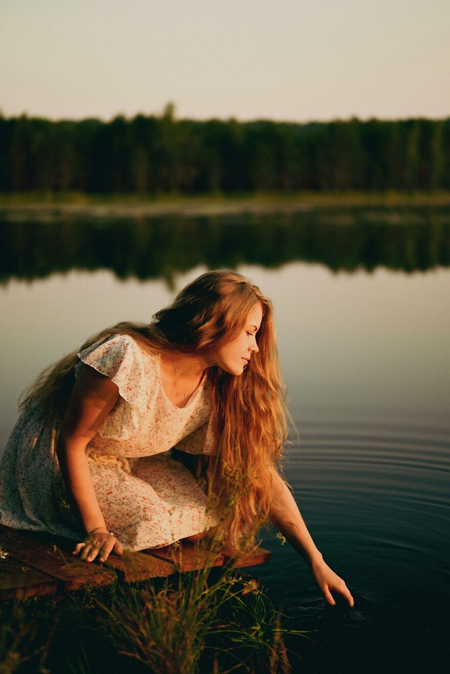 Young woman with long hair touching calm water by the lake, reflecting on the value of the earth planet.