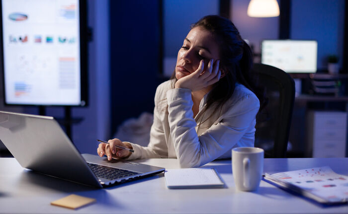 Woman showing frustration working late on a laptop highlighting pointless infuriating bizarre office rules at night.