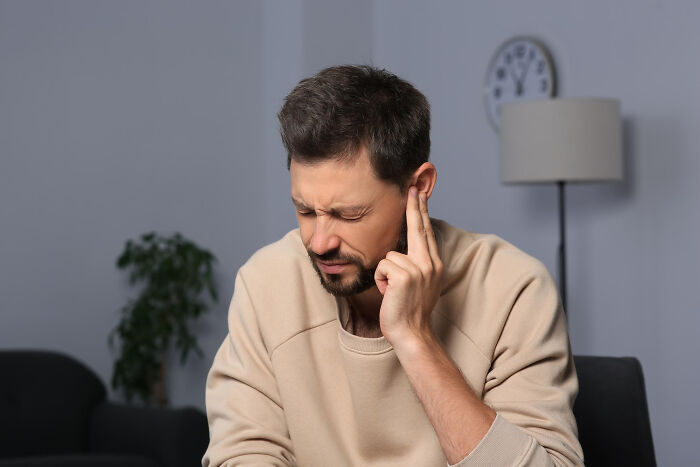 Man sitting indoors, wincing in discomfort, touching his ear experiencing wait thats not normal moments.