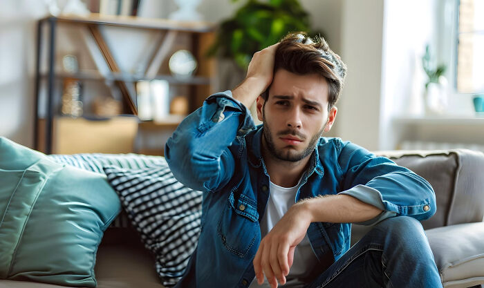 Young man sitting on couch with worried expression, distressed after mom discovered cheating on girlfriend.