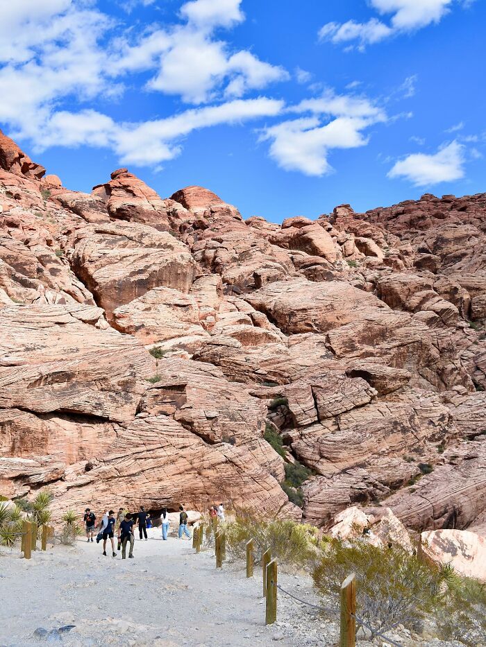 Visitors walk along a trail with red rock formations under a bright blue sky at Red Rock Canyon in a viral tourist incident.
