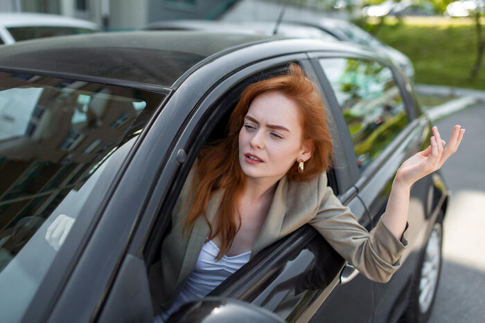 Red-haired woman sitting in car looking confused and frustrated, capturing a moment so ridiculous people thought they were pranked.