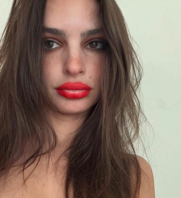 Emily Ratajkowski close-up portrait with red lipstick and long brown hair, linked to hijab disrespect controversy.