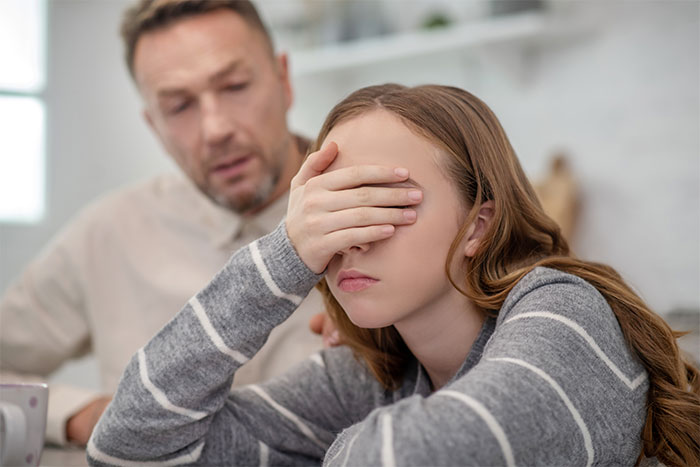 Teen girl upset and covering her face while a man looks on, depicting a story about refusal to give money. Teen girl upset and covering her face while a man looks on, depicting a story about refusal to give money.