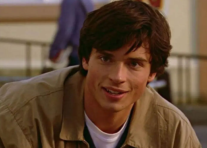 Young man with dark hair wearing a tan jacket smiling, representing 2000s teen heartthrob appearance at 48.