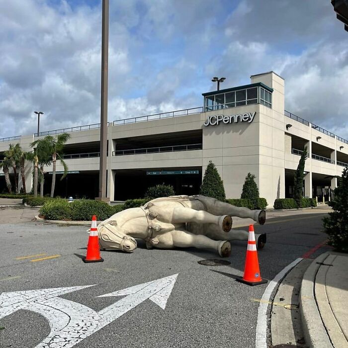 Large fallen statue lying in street near parking garage, surrounded by traffic cones, showing weirdest things found in streets.