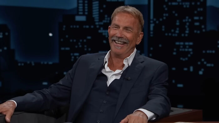 Man in a dark suit smiling during a talk show interview about meeting idols and regretting it shared online.