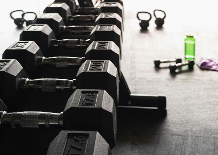 Row of gym dumbbells with a 25-pound weight visible, kettlebells and fitness gear in the background during a gym fight incident.