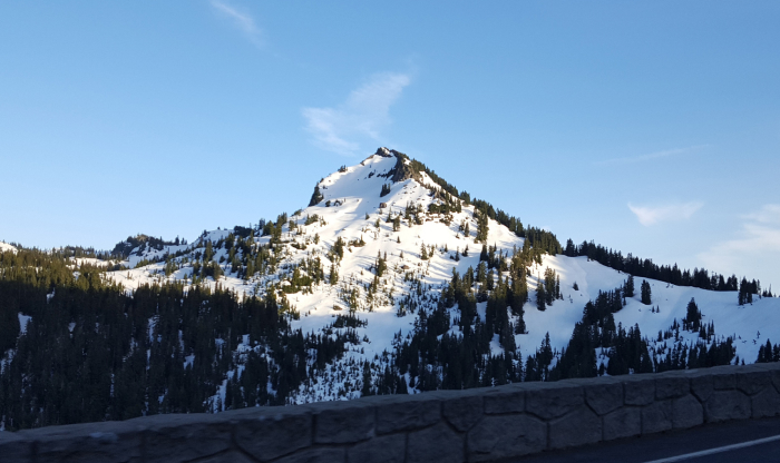 Snow-covered mountain with dense forest below under clear blue sky, illustrating haunted places in America&rsquo;s eerie landscapes.