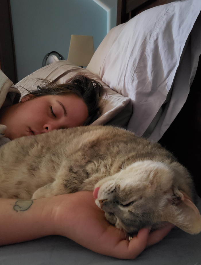 Woman sleeping peacefully in bed with a cat resting on her arm, illustrating sleep needs of women versus men.