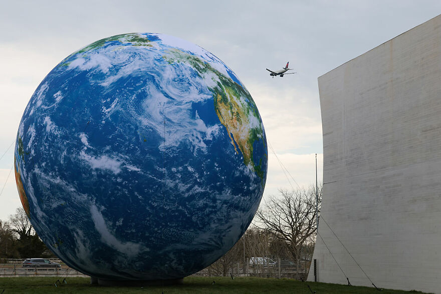 Large Earth model outdoors with an airplane flying overhead, illustrating concepts of planet value and Earth costs.