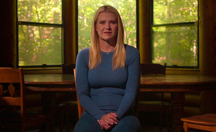 A woman sitting in a dimly lit room with large windows, featured in Elizabeth Smart Netflix documentary Kidnapped.