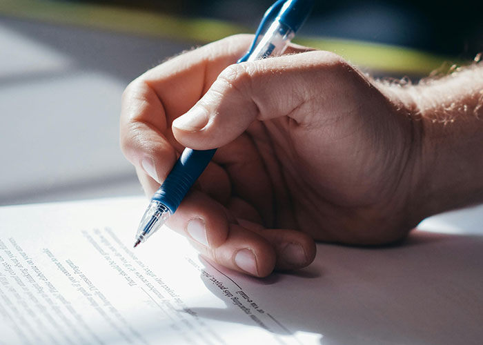 Close-up of a hand holding a pen and writing on a document representing perfect revenge acts that remain unnoticed.