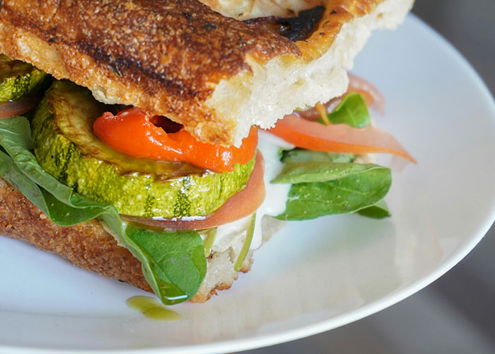 Close-up of a vegetable sandwich with zucchini and greens on a white plate, illustrating perfect revenge acts concept.