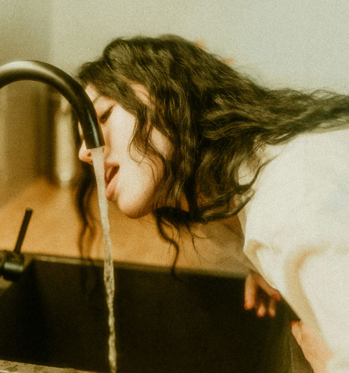 Woman with long curly hair drinking water from a faucet, symbolizing little things that made sense after cheating revealed phone use