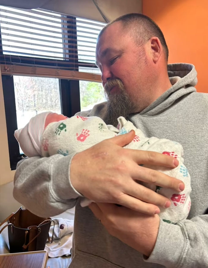 Father holding newborn baby, reflecting on family impact as 15-year-old gets pregnant with 12-year-old’s child.