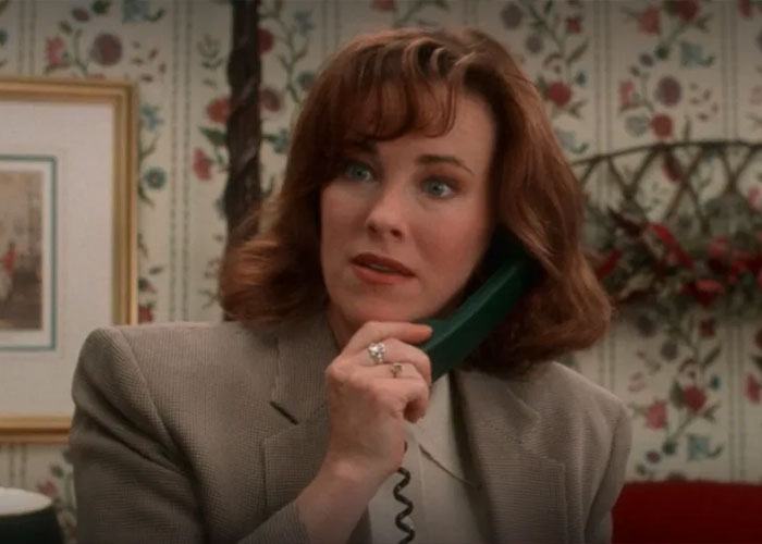 Schitt’s Creek star Catherine O'Hara with red hair and blazer talking on a green landline phone indoors. Schitt’s Creek star Catherine O'Hara with red hair and blazer talking on a green landline phone indoors.