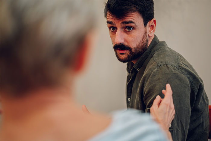 Man listens intently while an older woman speaks, depicting tension related to finances and family conflict.