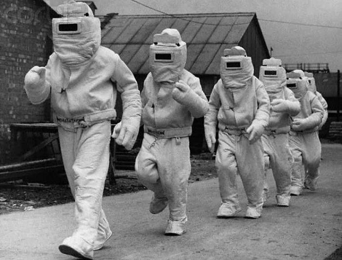 Group of people in old black and white protective suits walking outdoors, showcasing odd and creepy vintage imagery.