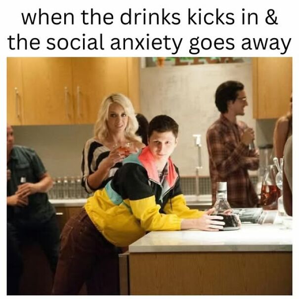 Young man at a party leaning on a counter with a drink, illustrating relatable memes about social anxiety and drinking.