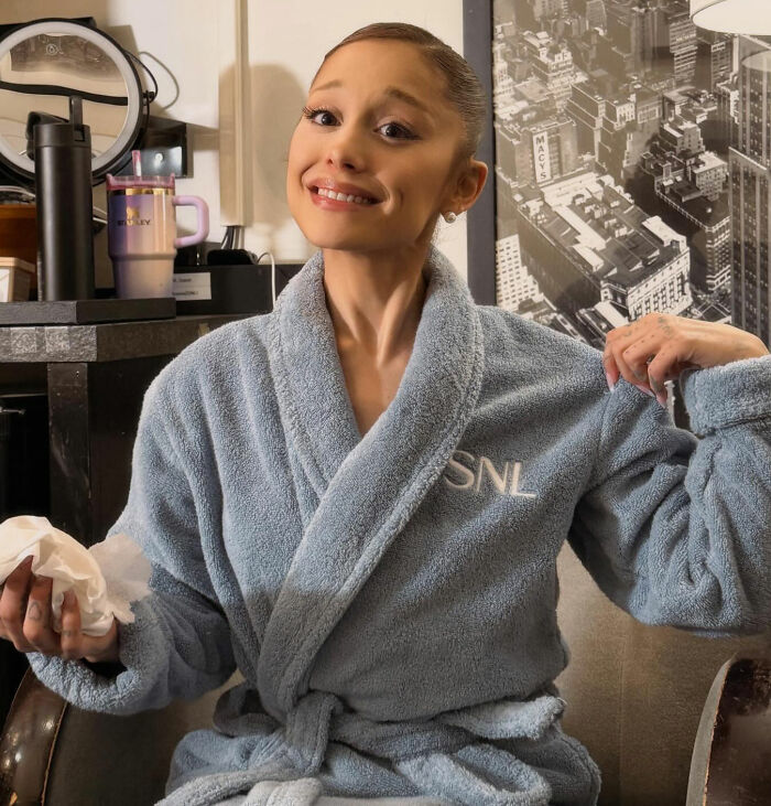 Ariana Grande in a blue SNL robe with a peculiar expression, sparking theories about her bizarre mannerisms.