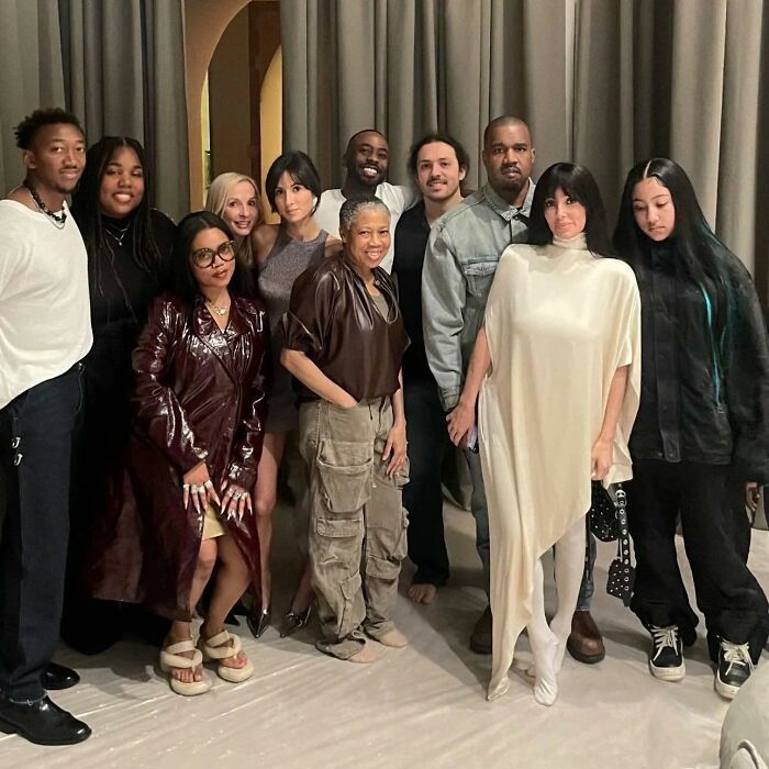 North West with a sad expression standing in a family photo with Bianca Censori and others indoors.