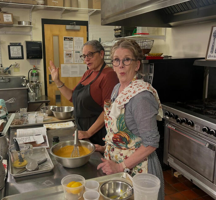 Two women in aprons prepare food in a kitchen, relating to Melissa Gilbert sparks outrage Instagram fridge tour.
