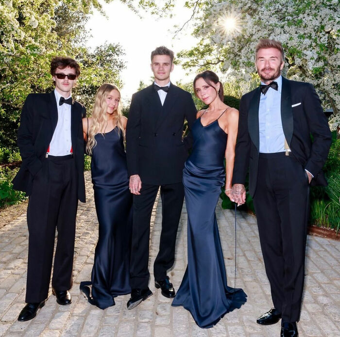 Brooklyn Beckham with parents David and Victoria Beckham and siblings dressed formally outdoors in a garden setting.