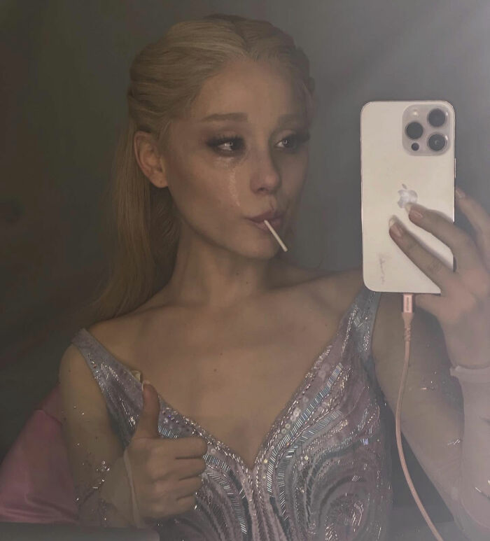 Ariana Grande taking a selfie with a smartphone, showing bizarre mannerisms and an unsettling expression.