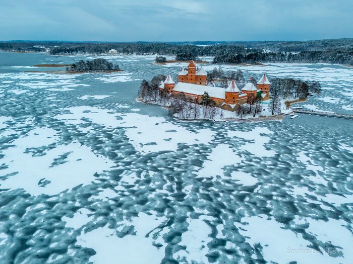Imagen acogedora de invierno con castillo cubierto de nieve rodeado de lago congelado y paisaje frío y sereno.