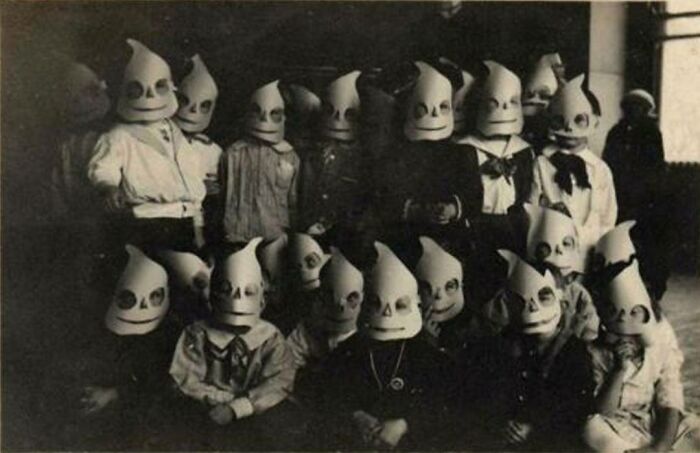 Group of children wearing odd and creepy masks in an old black and white photo, creating an eerie atmosphere.
