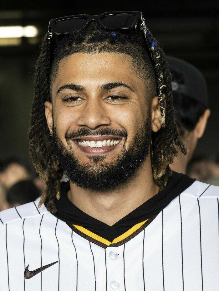 Fernando Tat&iacute;s Jr. smiling, wearing a striped baseball jersey and sunglasses on his head at a public event.