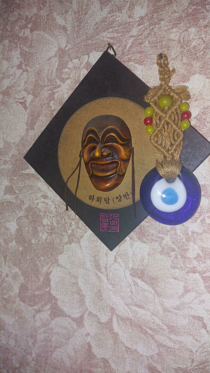 Wooden creepy mask and evil eye charm hanging on textured wall, capturing interesting but creepy vibes.