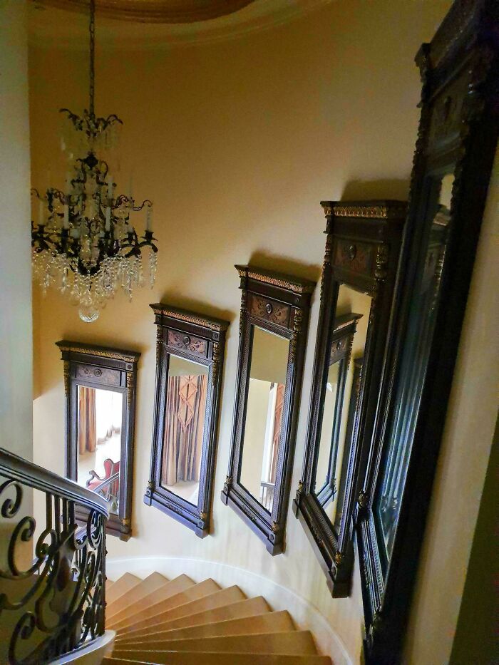 Spiral staircase with tilted antique mirrors creating a distorted and creepy visual effect inside the house.