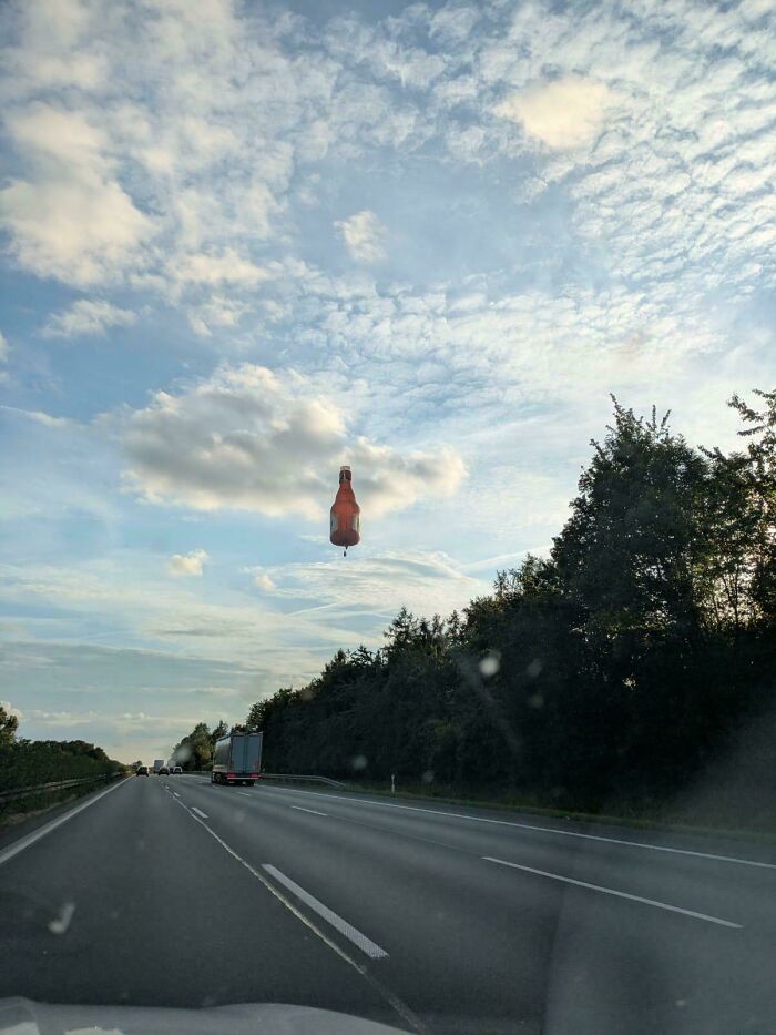 Hot air balloon shaped like a beer bottle flying over a highway, showcasing impressive things countries implemented.