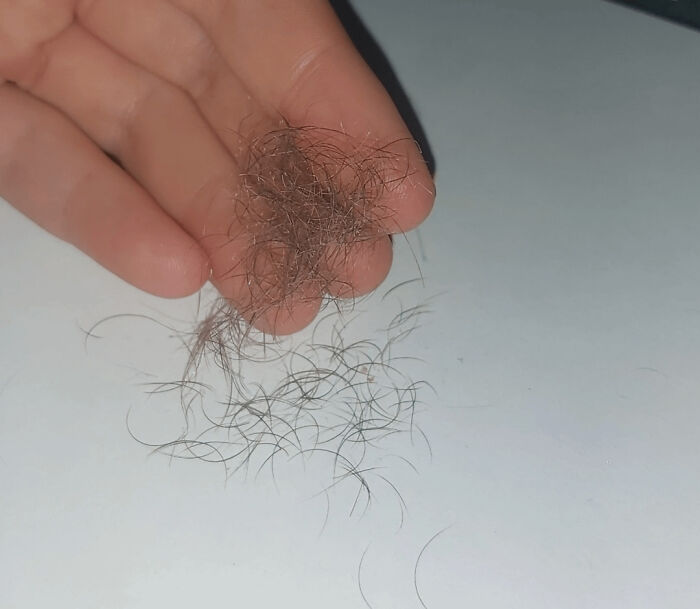 Hand holding a cluster of tangled hair strands on a white surface, illustrating an interesting but creepy visual.