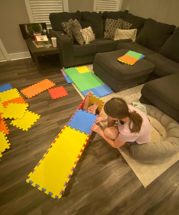 Two siblings playing with colorful foam puzzle mats in a living room, showing how life is more fun with siblings.