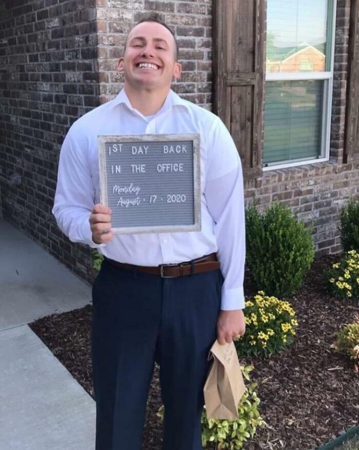 Smiling man holding a sign on first day back in the office, illustrating life is more fun with siblings.