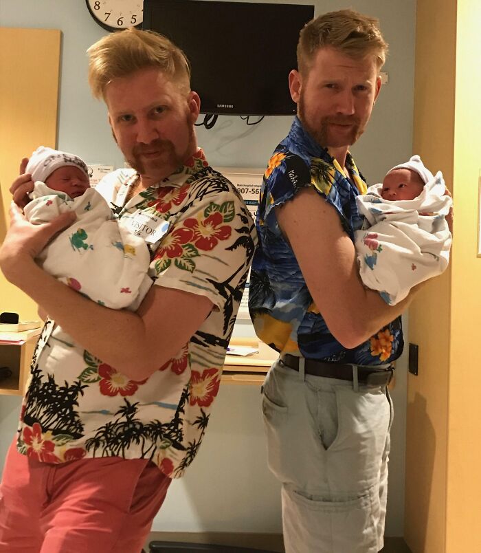 Two men holding newborn babies in a hospital room, showcasing joyful sibling moments and family fun together.