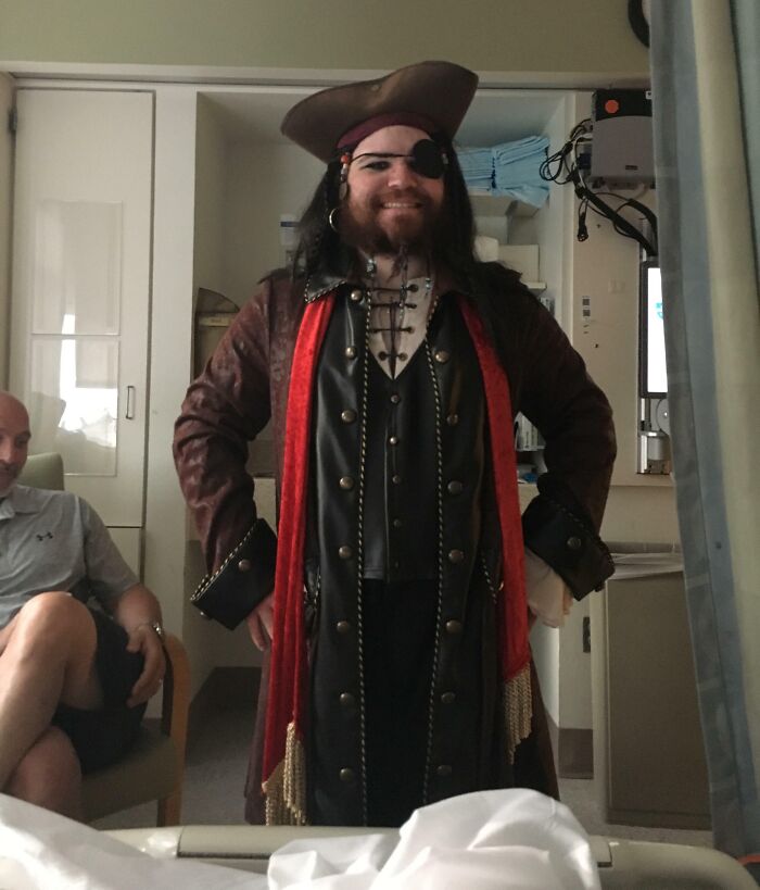 Man dressed as a pirate smiling in a room while another person watches, showing fun sibling moments and playful costumes.