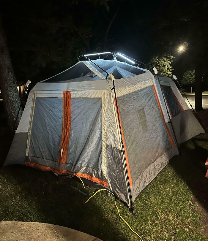 Large camping tent illuminated at night on grass, showing outdoor adventure and fun with siblings concept.