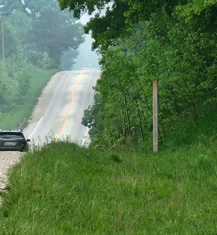 Car parked partly on rural road shoulder beside trees on hilly country lane, illustrating next-level jerks