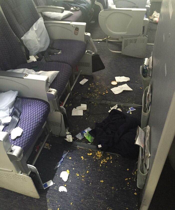 Messy airplane cabin with trash and spilled snacks on floor, scene of next-level jerks.